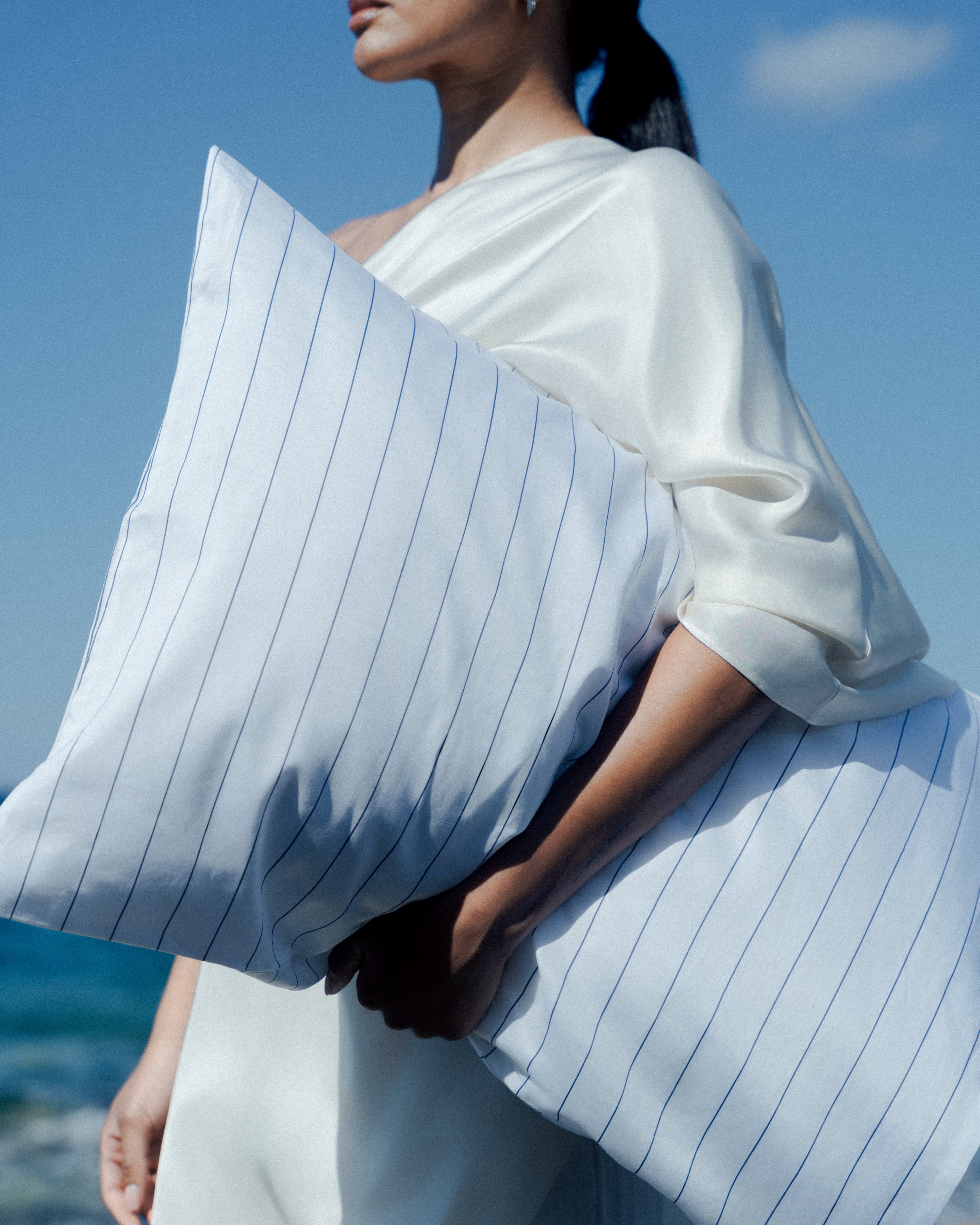 Woman holding a light blue striped pillow with a beautiful blue background