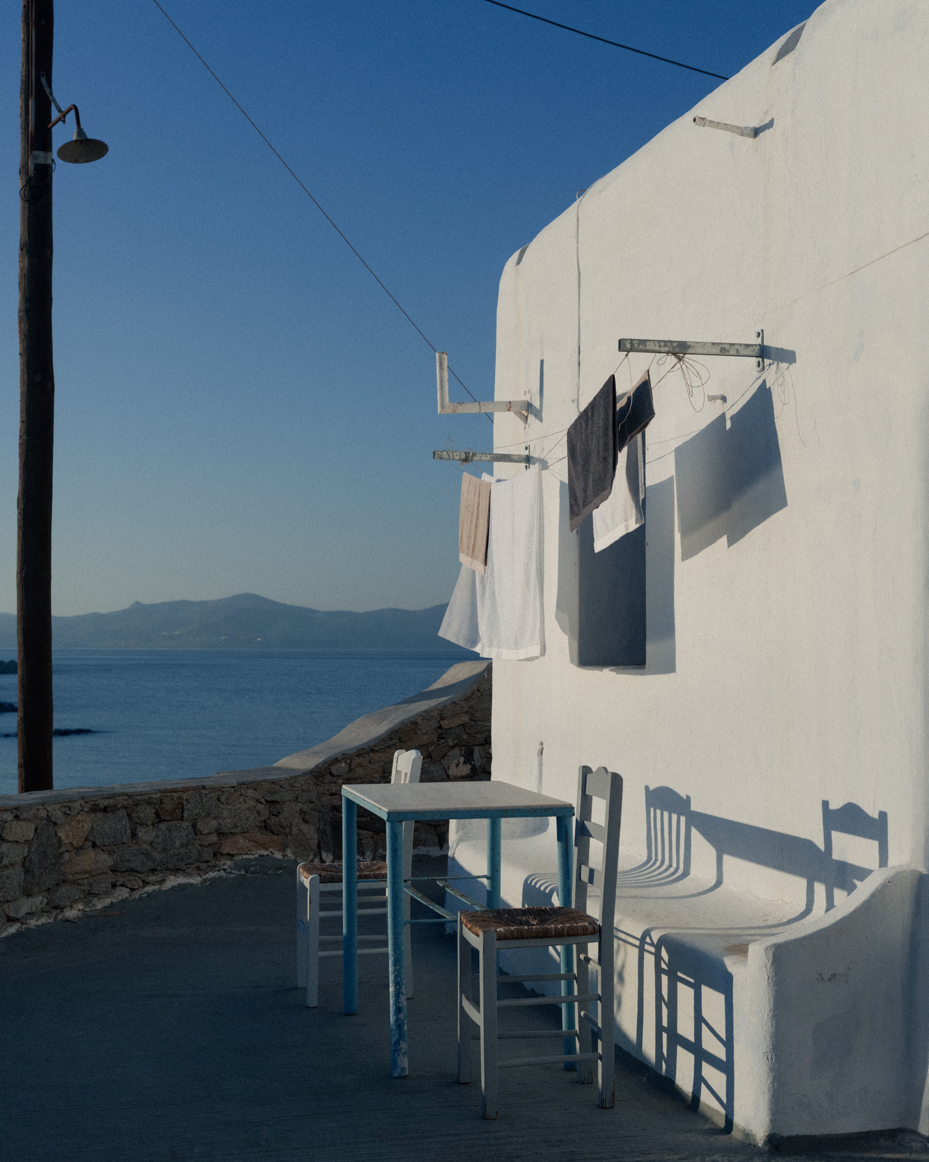 picture of a white building in front of the blue ocean in Mykonos. A few Abate towels are hanging from clothing lines.